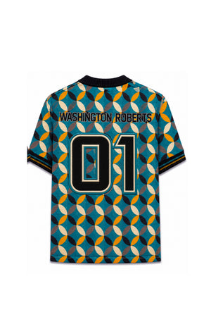 A folded V-neck knit sweater from Washington Motorsports on a wooden floor. The sweater features a teal blue background with a repeating geometric pattern of black, white, brown, and orange ovals.